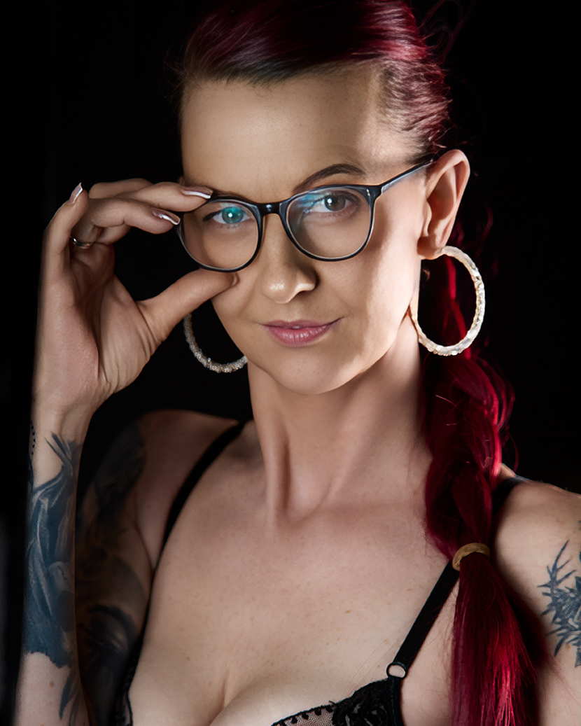 Portrait einer Frau mit rotem Haar und Brille vor schwarzem Hintergrund